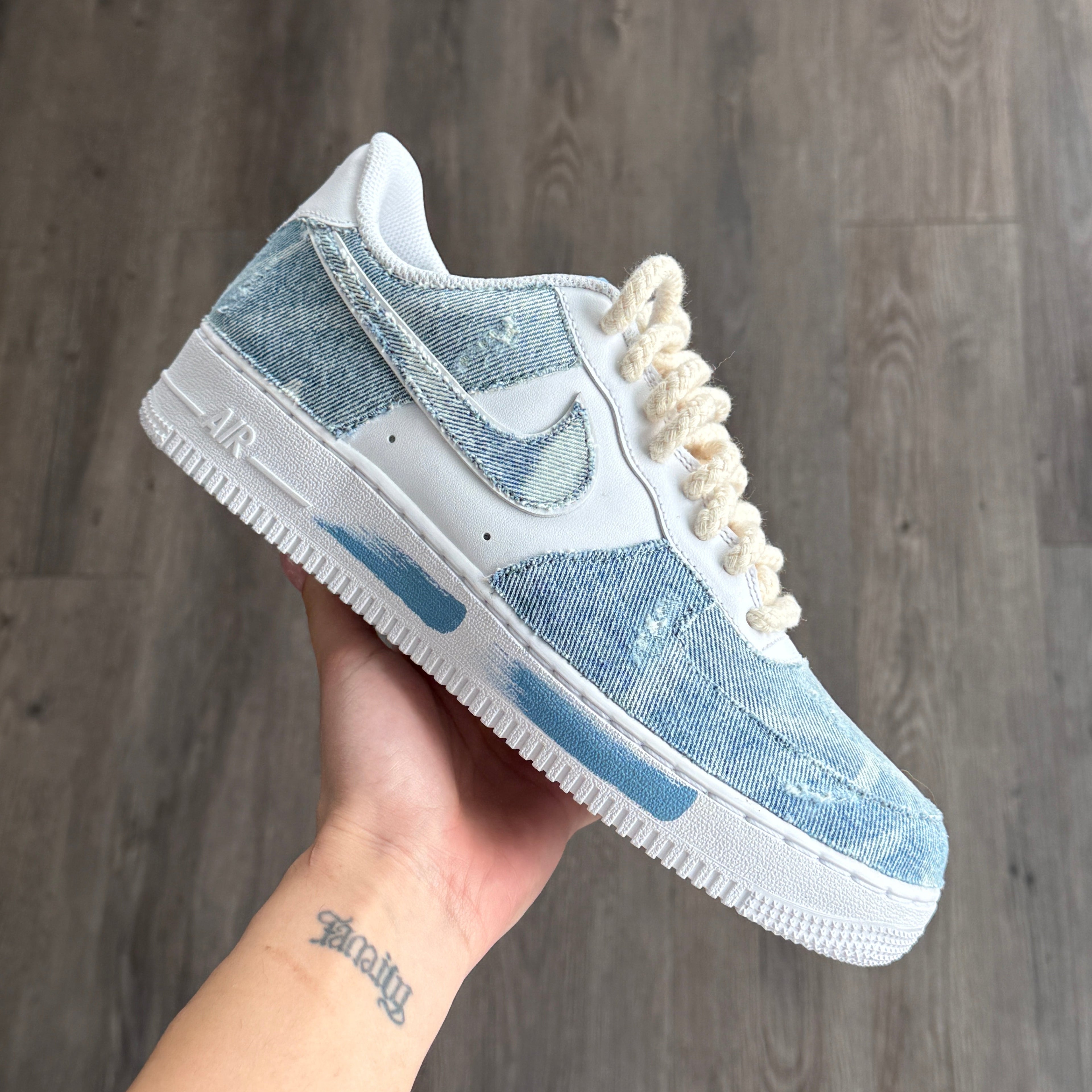 Blue and white sneaker with decorative elements held by a hand on a wooden floor.