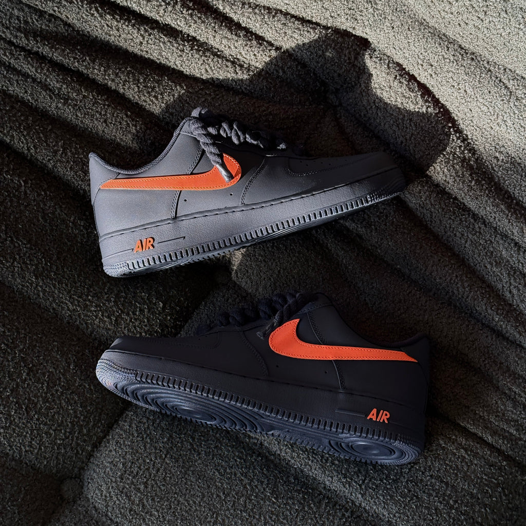 Pair of black and gray sneakers with orange accents on a textured surface