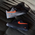 Pair of black and gray sneakers with orange accents on a textured surface