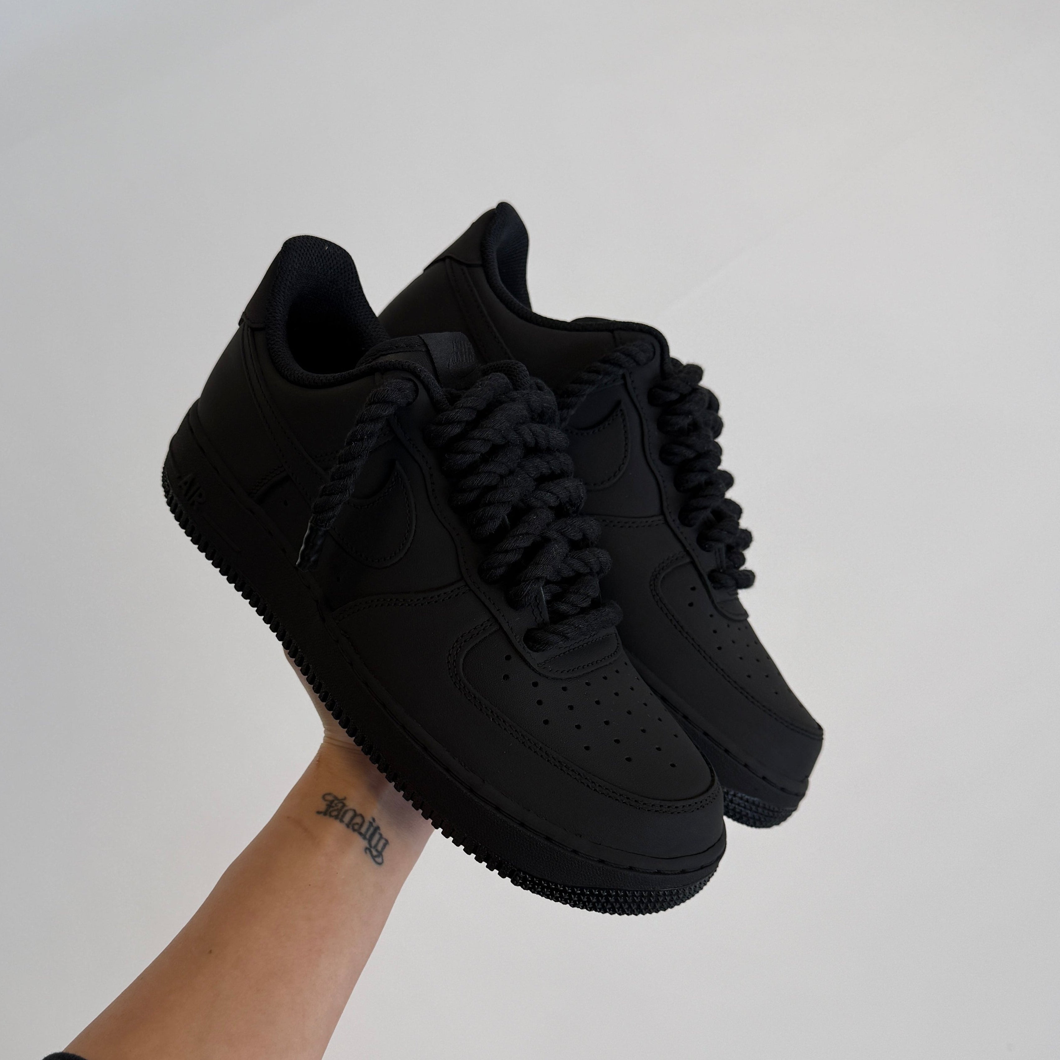 Person holding two black sneakers against a plain background