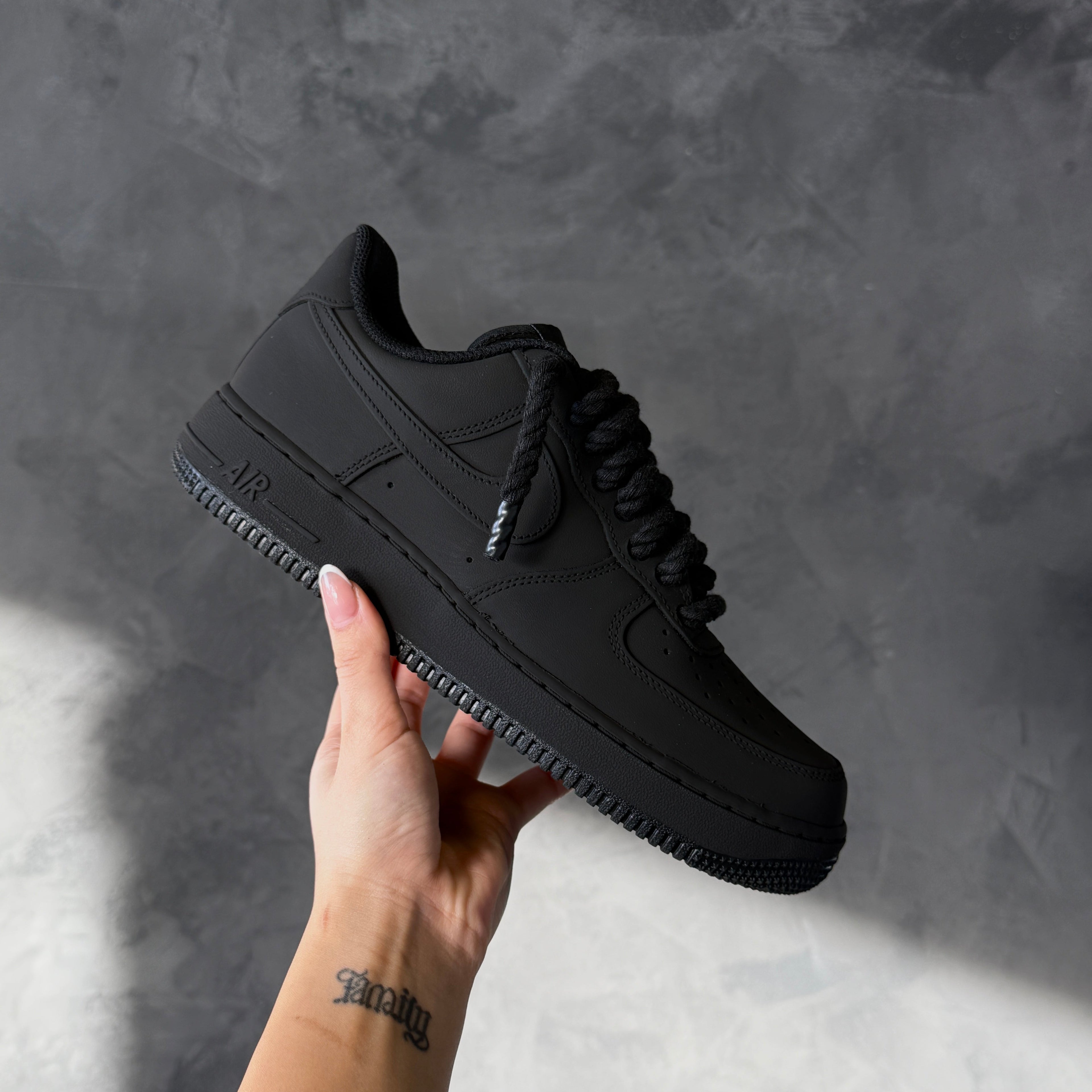 Black sneaker held by a hand against a gray background