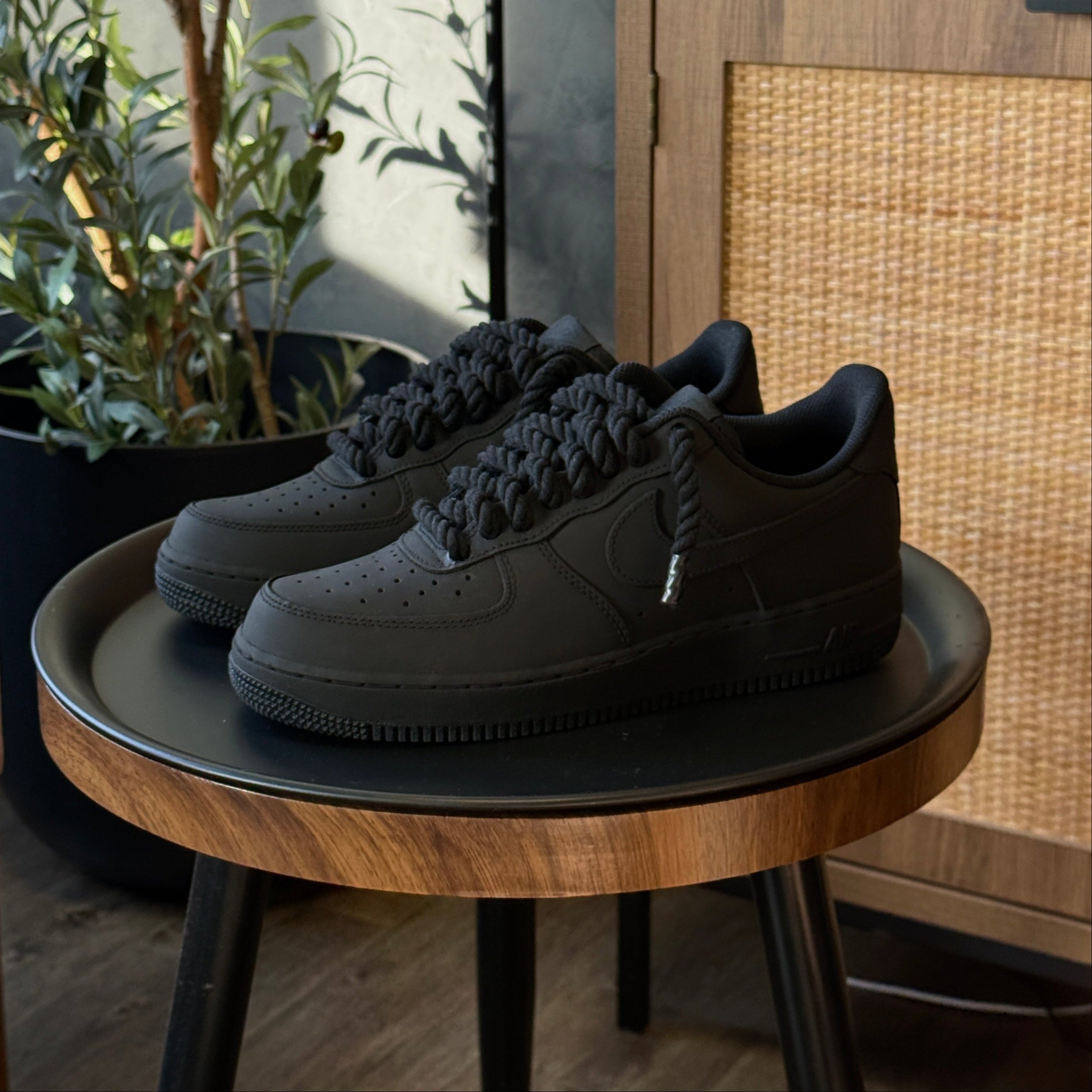 Black sneakers on a round wooden table with a plant and cabinet in the background