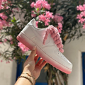 White sneaker with pink laces and sole held by a hand against a floral background